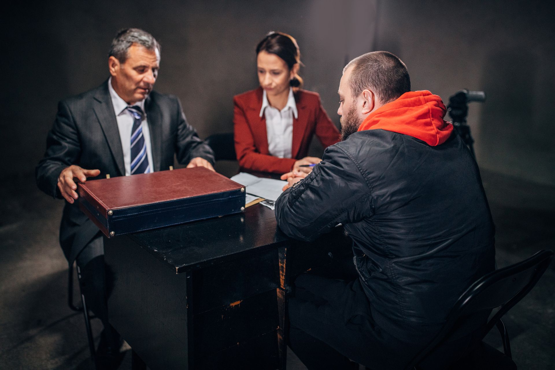 Man with handcuffs and two detectives/lawyer sitting in an investigation room. Man with handcuffs and two detectives/lawyer sitting in an investigation room.