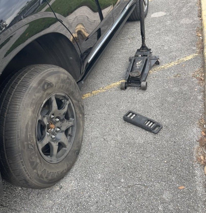A black car with a flat tire getting a tire change.
