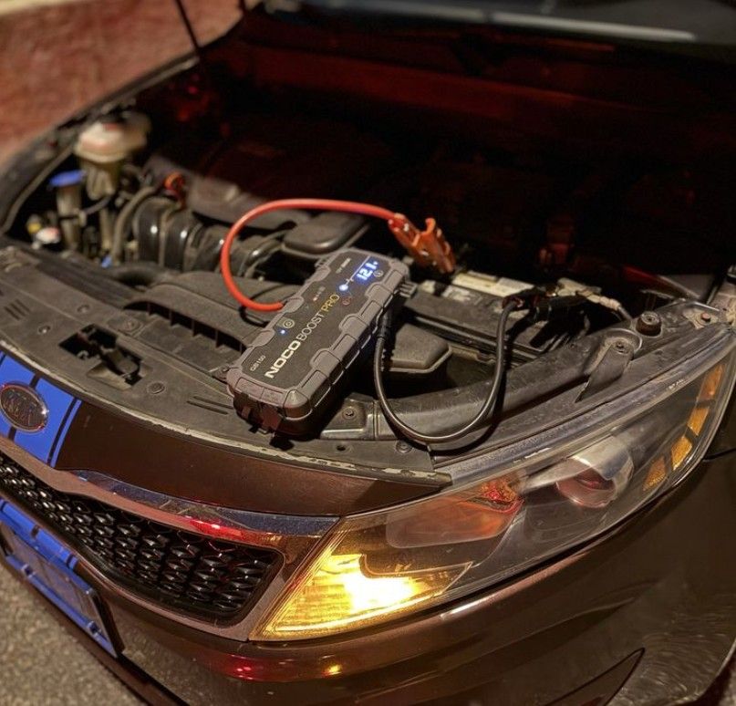 A black car with the hood open, getting a battery jumpstart.