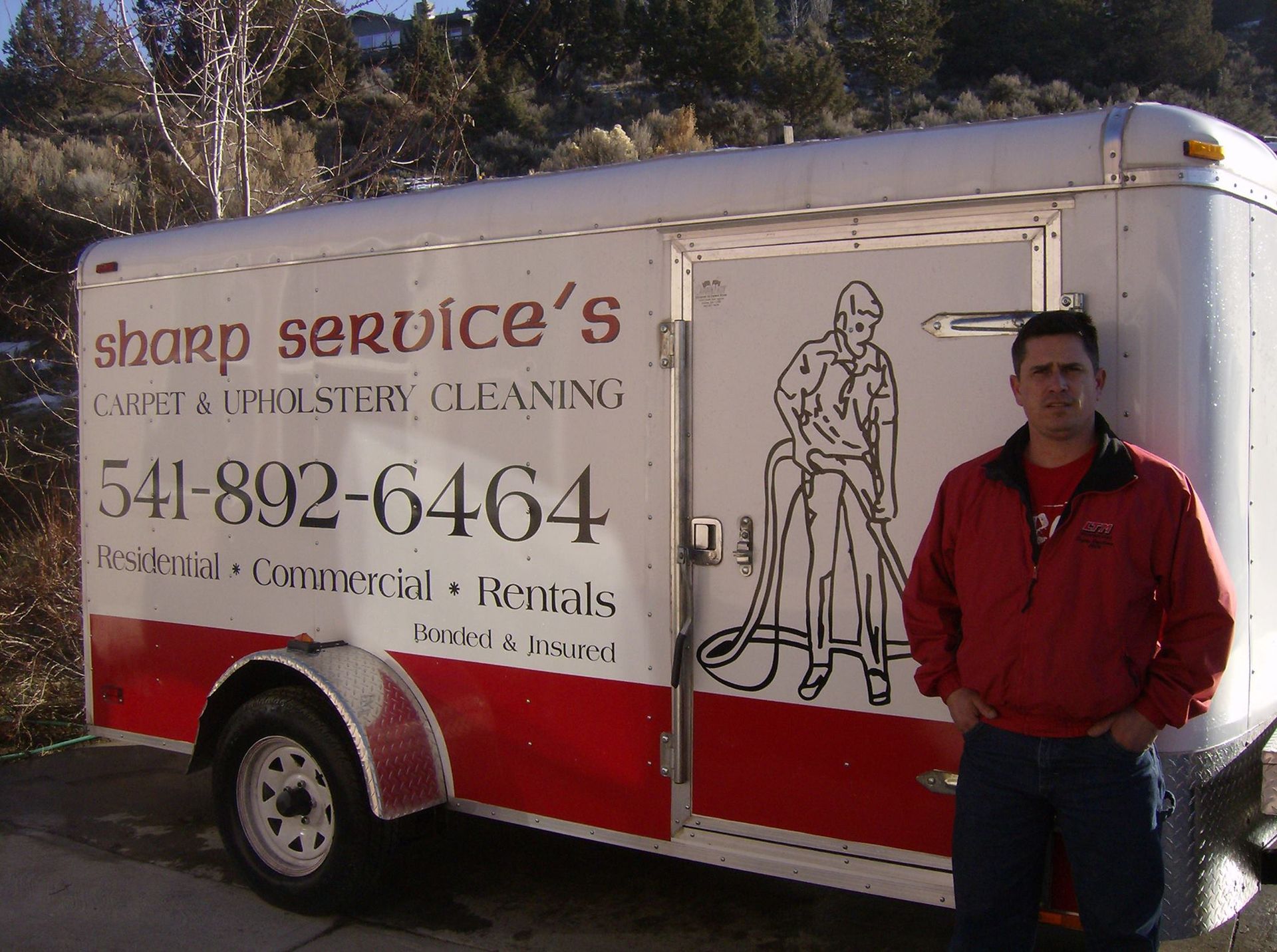 A man is cleaning a couch with a vacuum cleaner.