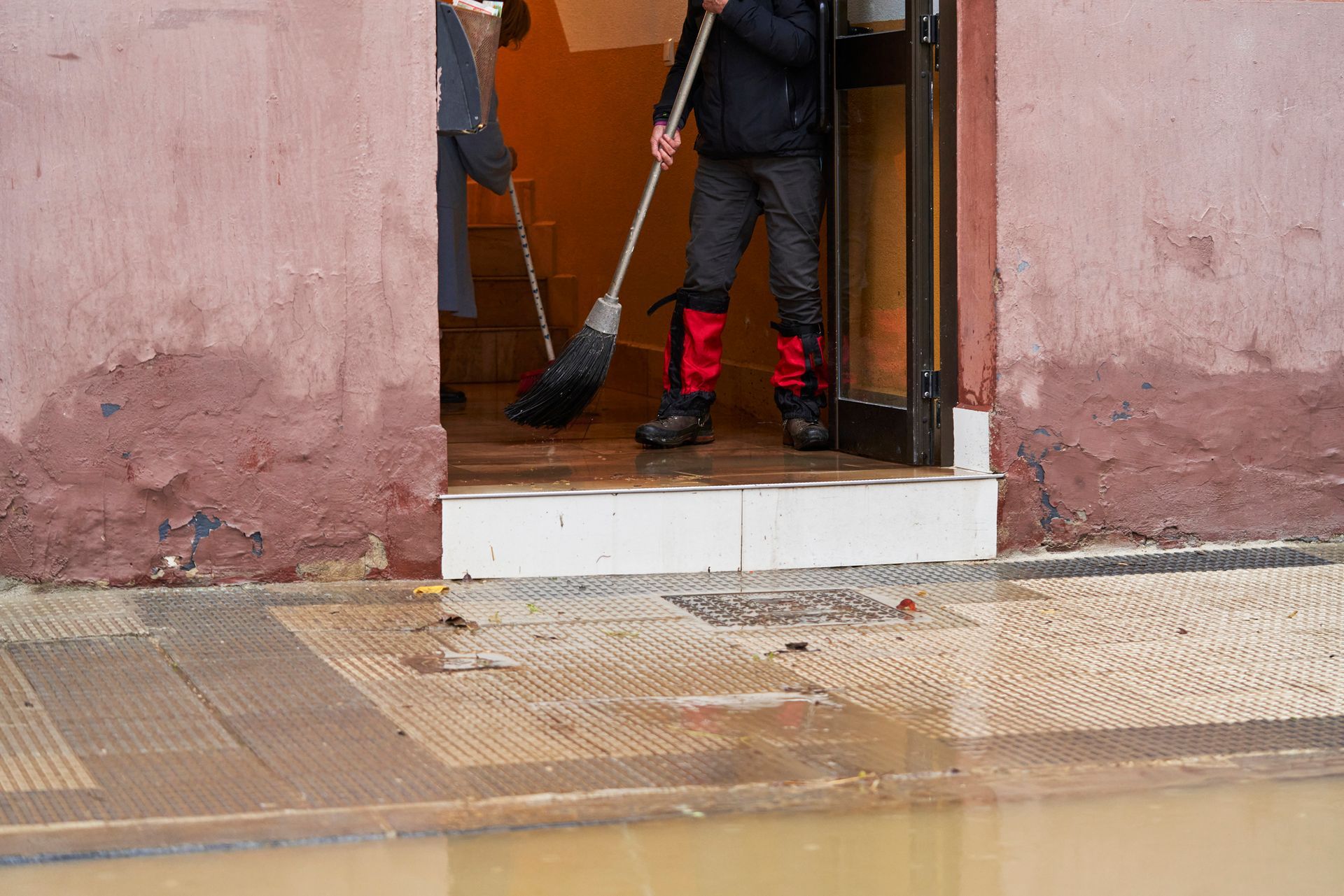 A person is cleaning a flooded doorway with a broom.