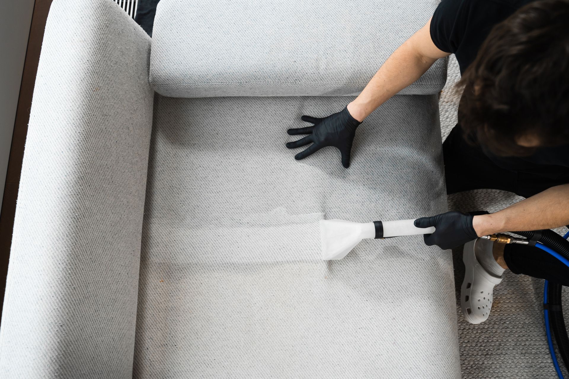 A woman is cleaning a couch with a vacuum cleaner.