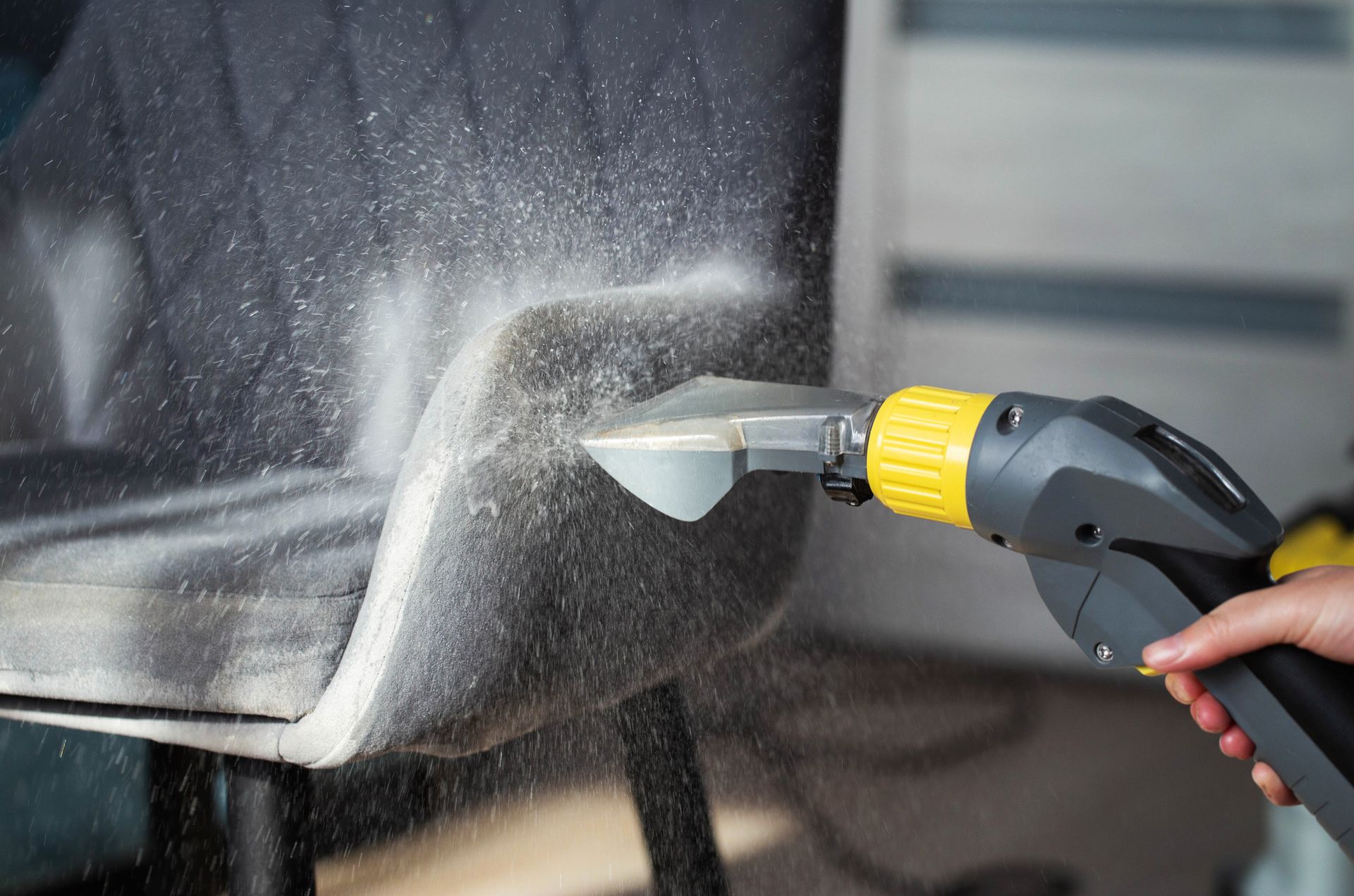 A person is cleaning a chair with a vacuum cleaner.