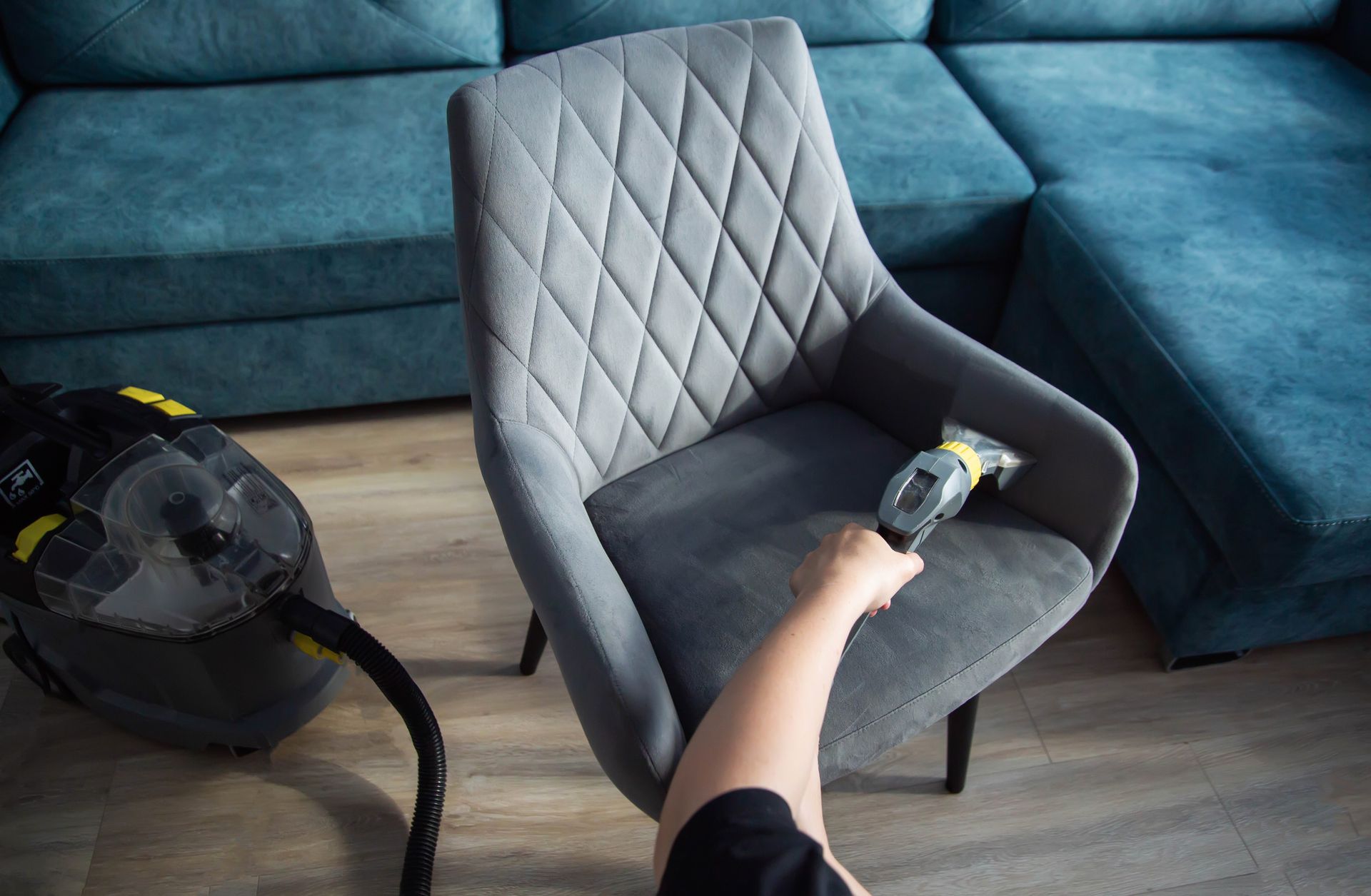 A person is cleaning a chair with a vacuum cleaner in a living room.
