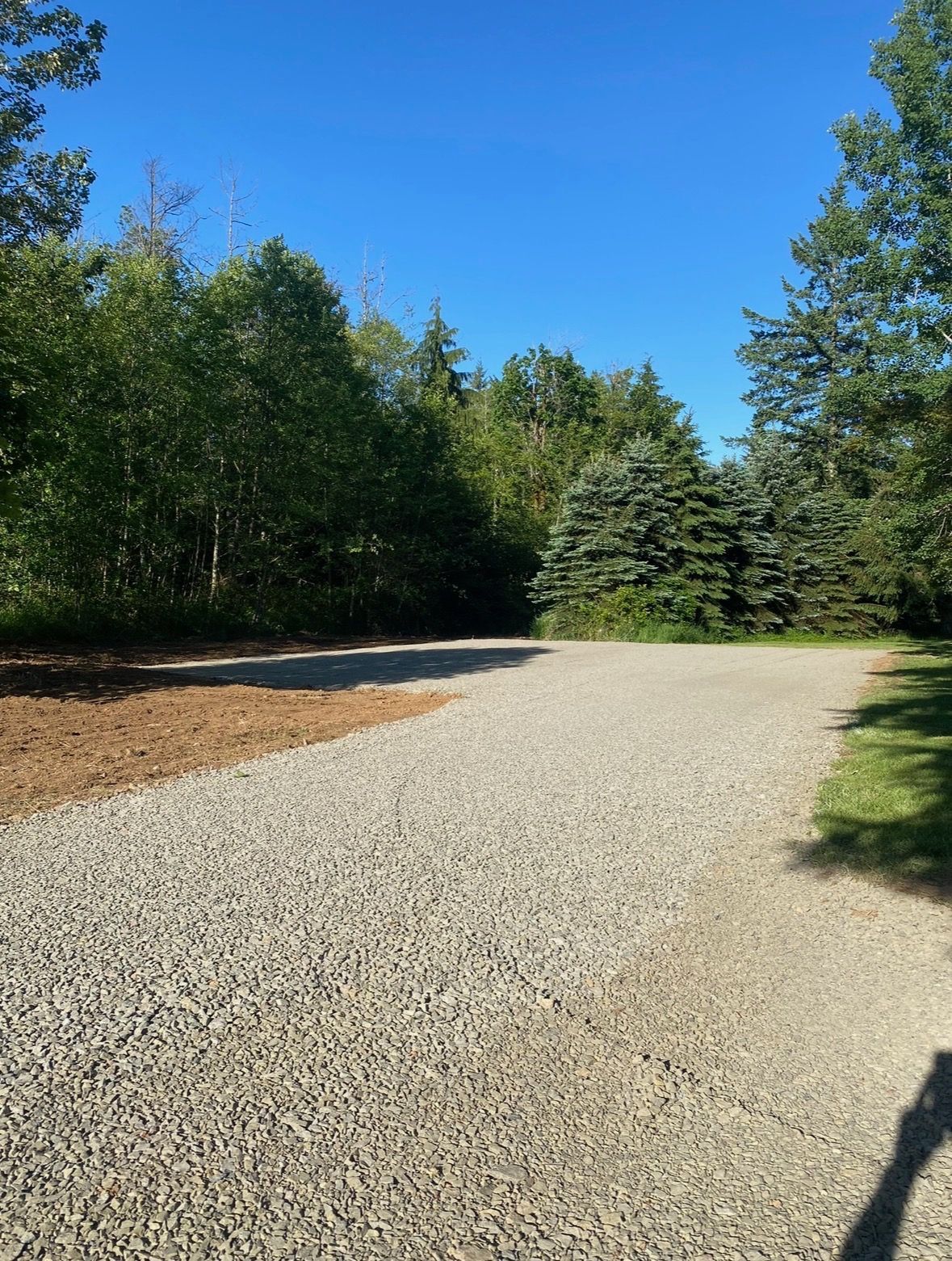 A rectangular construction site with a concrete foundation base, surrounded by gravel, heavy machinery, and dense forest.