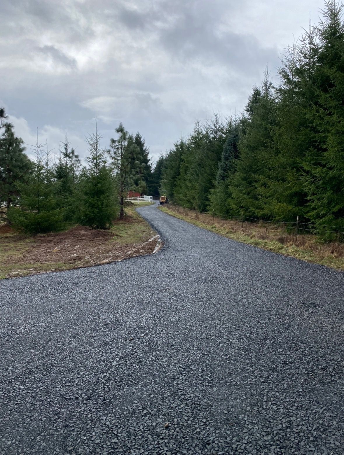 Aerial view of a gravel driveway loop under construction, surrounded by bare soil, garden beds, and a nearby building.