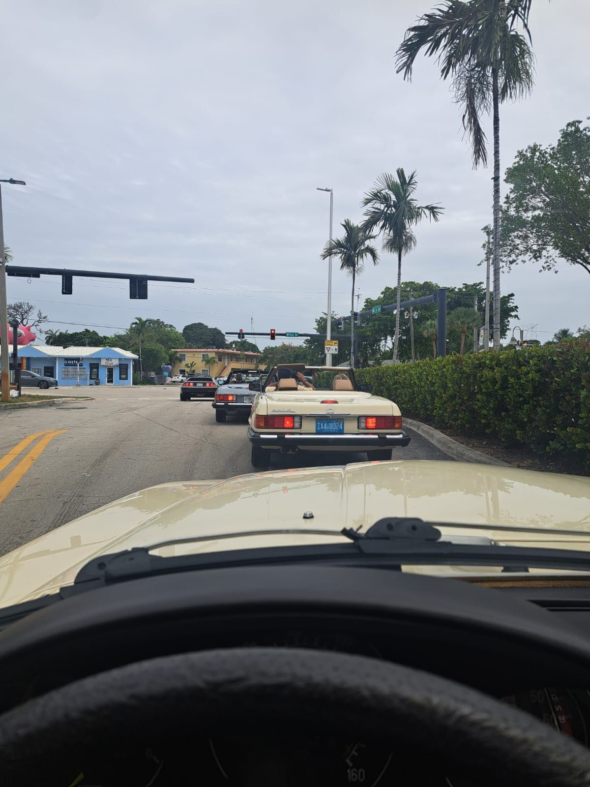 Traffic on a road with palm trees. Convertible cars stopped at a traffic light. Overcast sky.