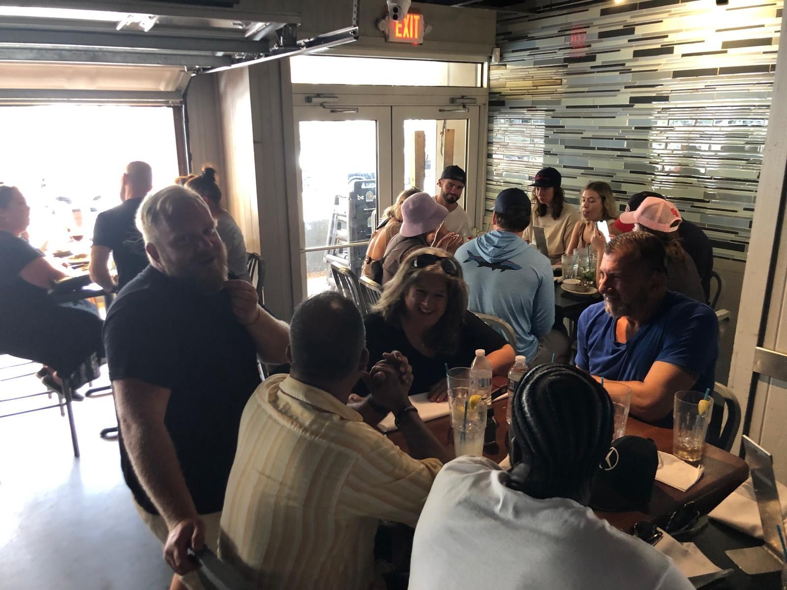 People at tables in an open-air restaurant; some are smiling and talking.