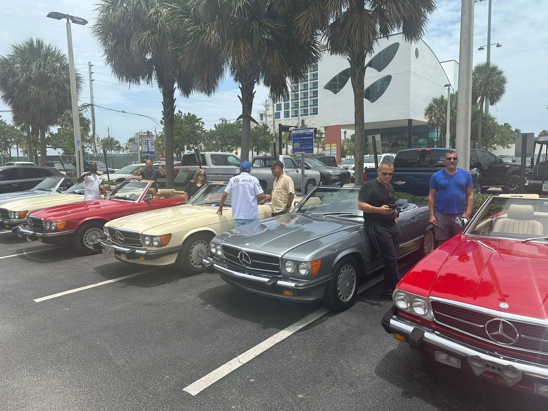 Classic convertible cars parked, men standing around, sunny outdoor setting.