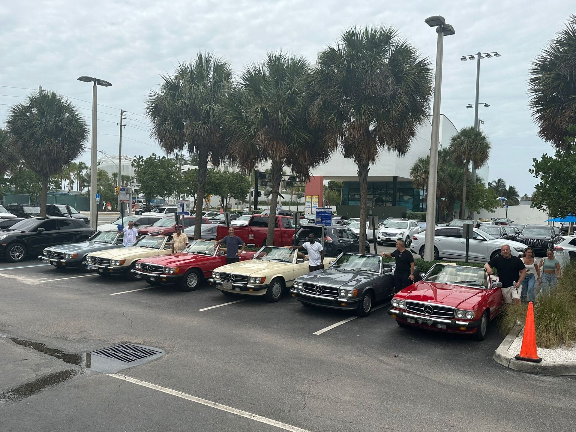Classic cars parked in a lot under a cloudy sky. People are standing nearby.
