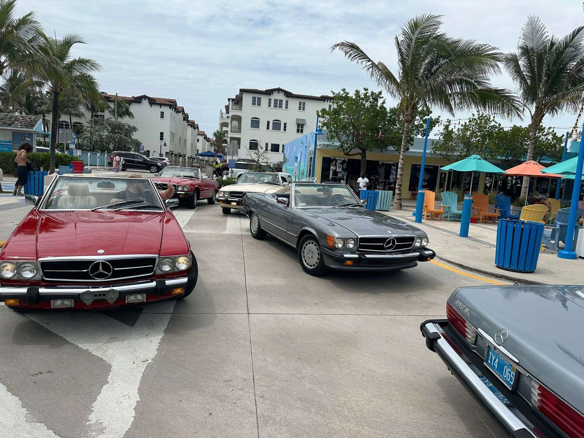 Classic Mercedes-Benz cars lined up on a street; red, silver and white vehicles. Palm trees and beach in background.