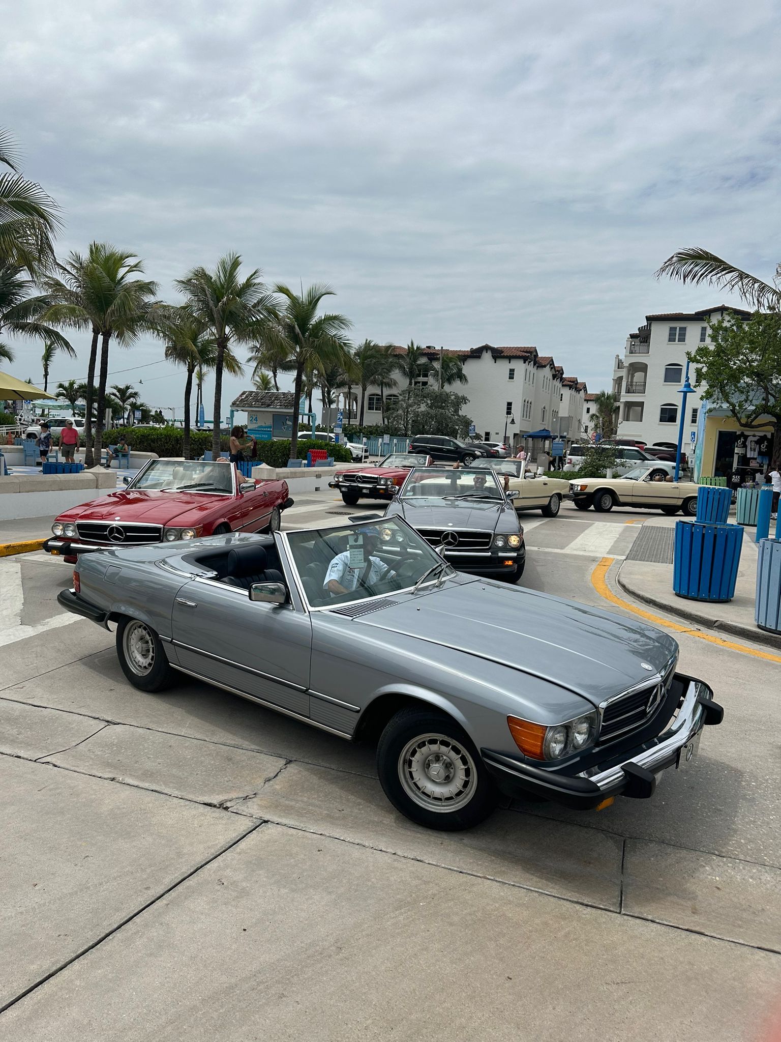 Silver convertible car parked on a street with other classic cars in front of buildings.