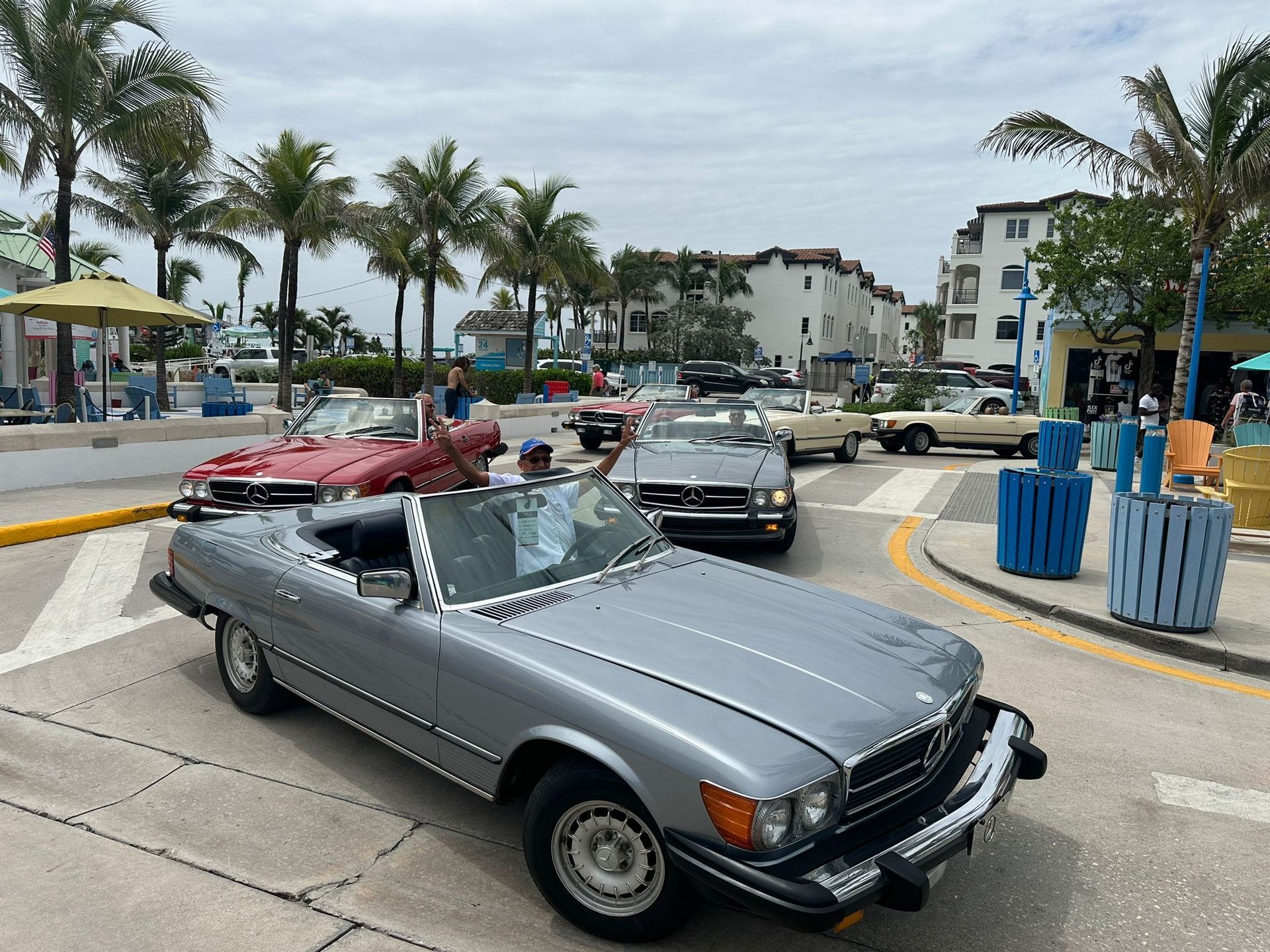 Classic convertible cars driving on a street lined with palm trees and buildings.