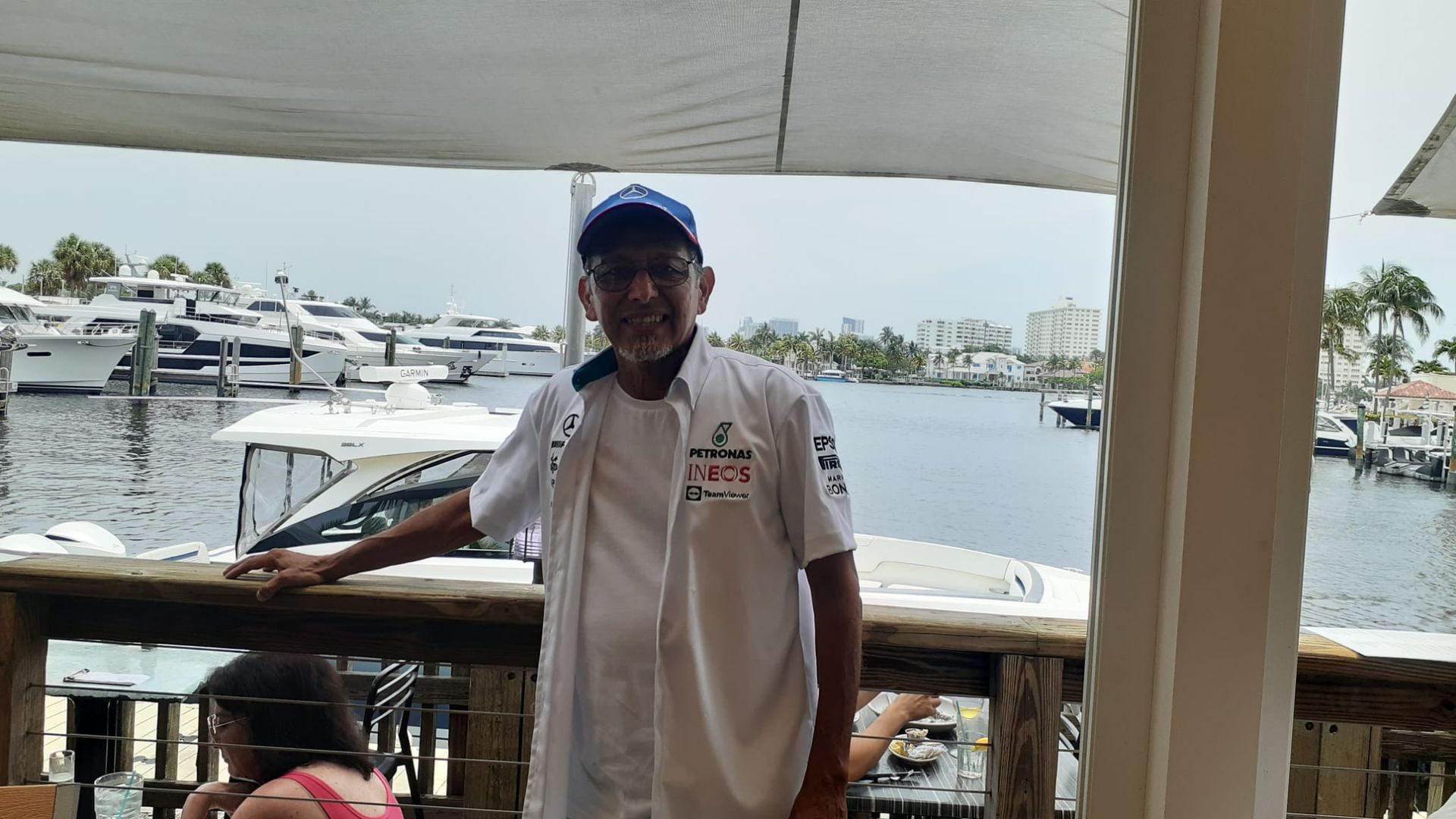 Person in white shirt and blue hat, standing on a deck overlooking a marina with boats.