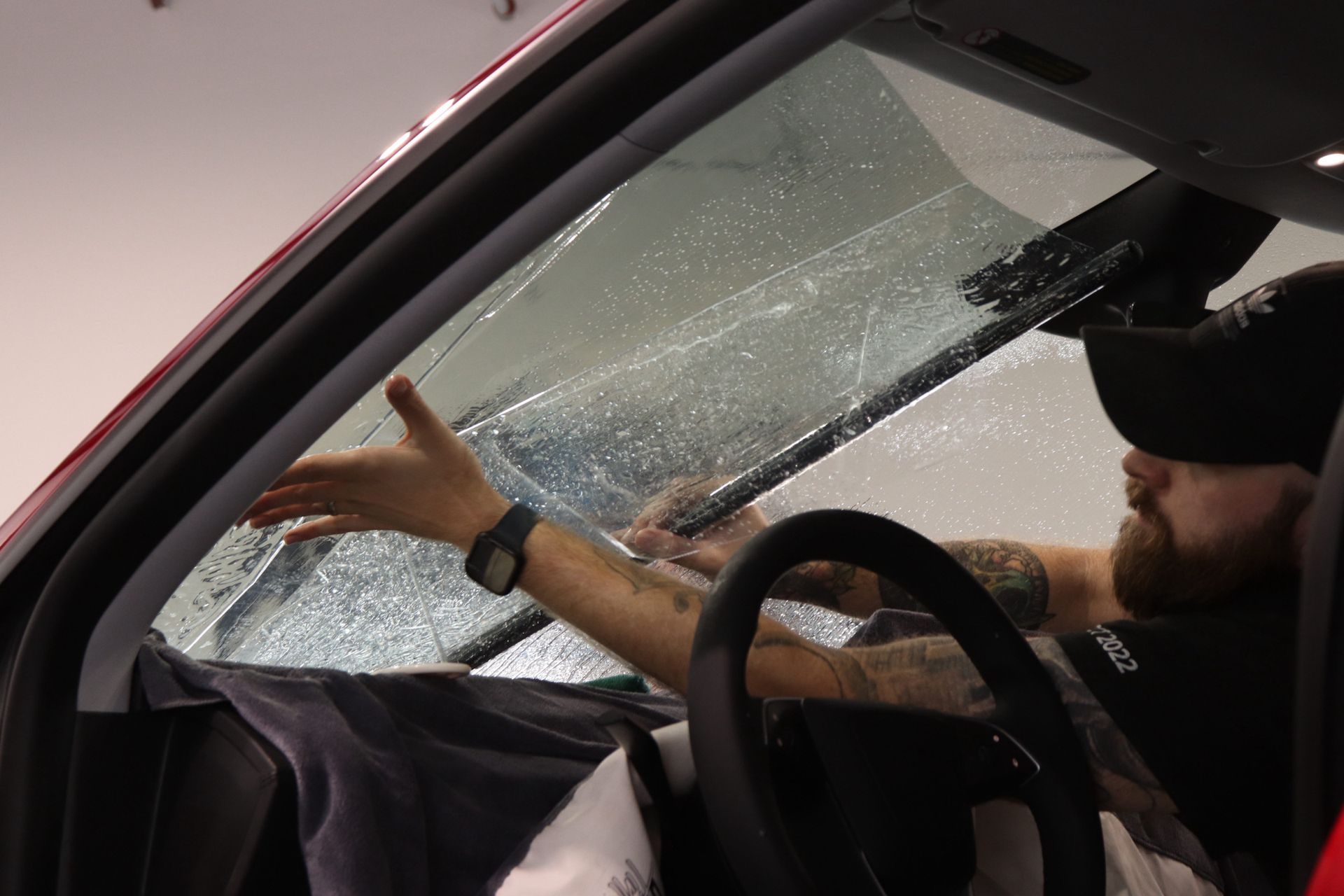 Man installing clear film on a car windshield inside a garage.
