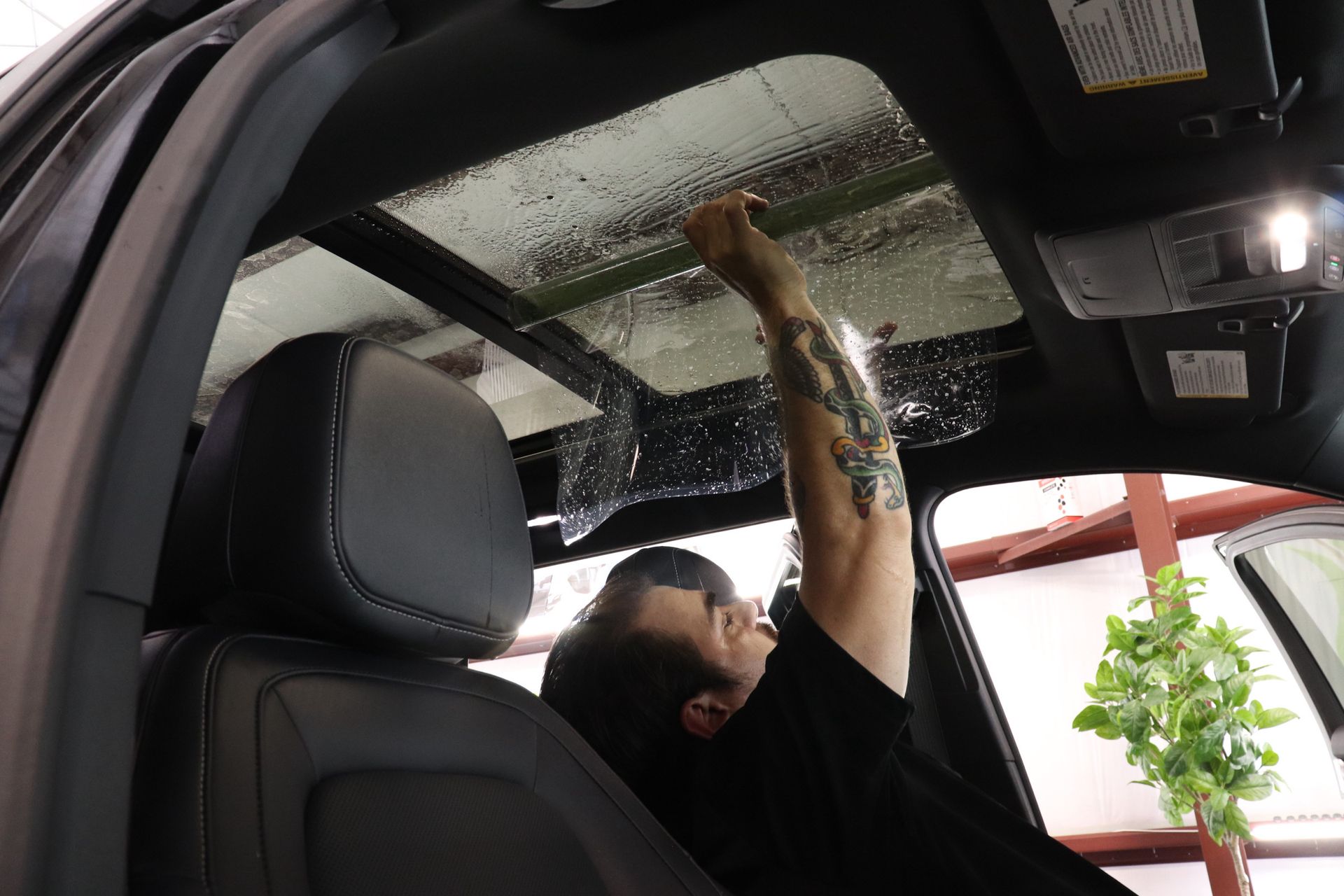 Person applying tint to a car's sunroof. Interior shot with a focus on the sunroof and the worker's arm.