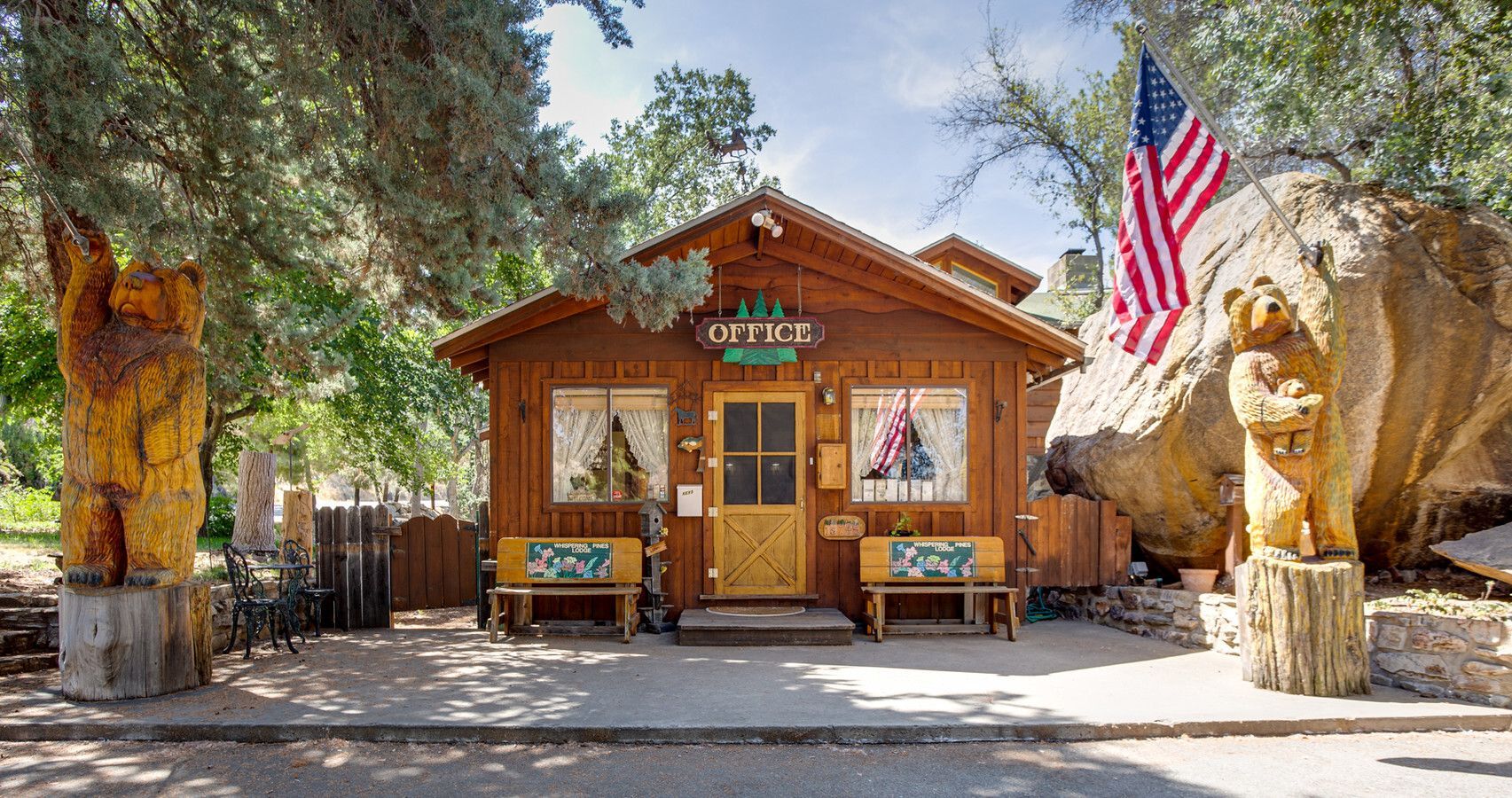 Wooden cabin with two benches, carved bear statues, and American flag.