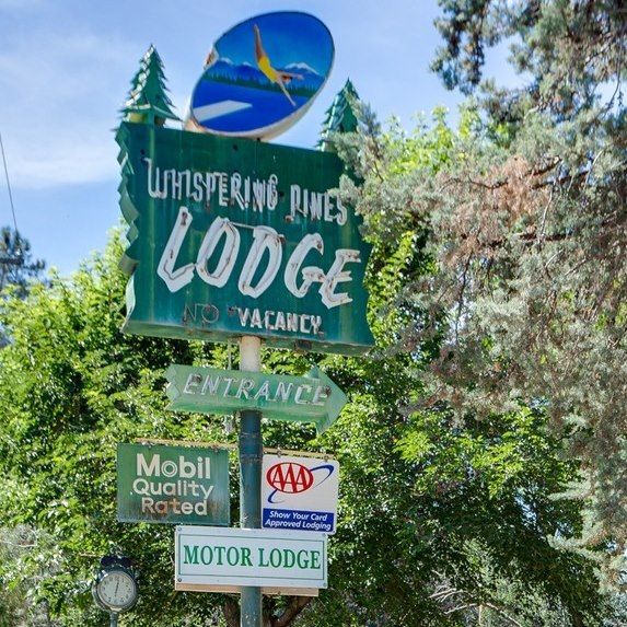 Sign for Whispering Pines Lodge with directional arrows and AAA and Mobil logos.