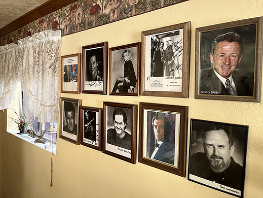 Wall with ten framed portraits, in a home setting. Portraits feature mostly men. Tan wall with a decorative border.
