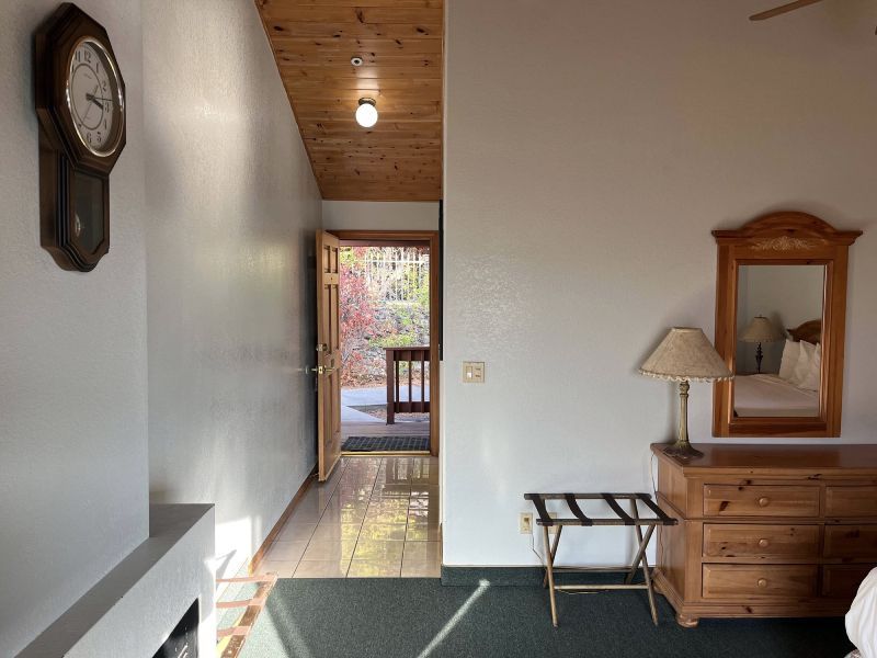 A motel room interior with a clock, a dresser with a mirror, and an open doorway leading to a patio.