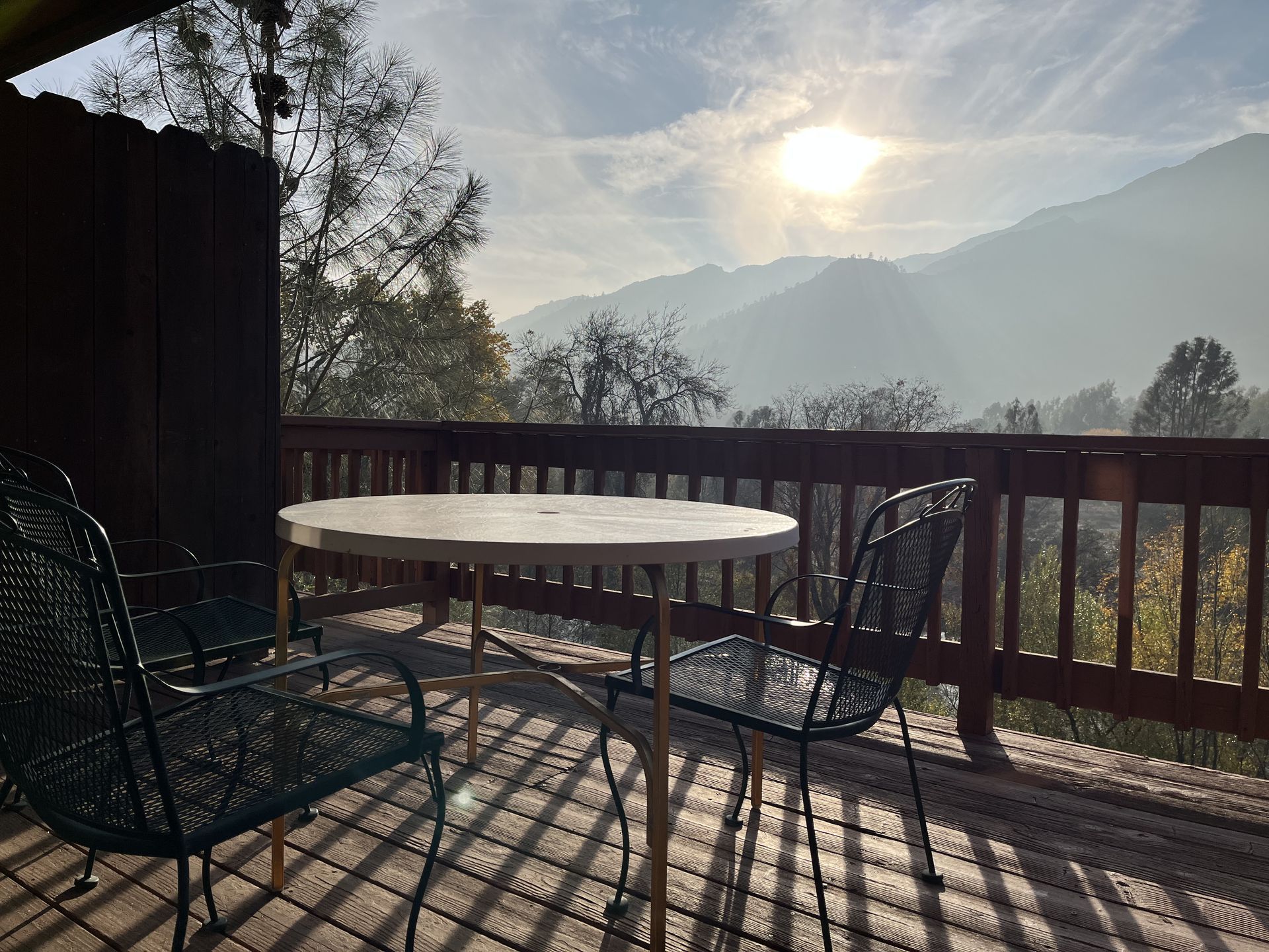 A deck with a table and chairs overlooking a mountain range under a sunny sky.