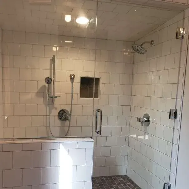 A bathroom with white tiles and a glass shower door.