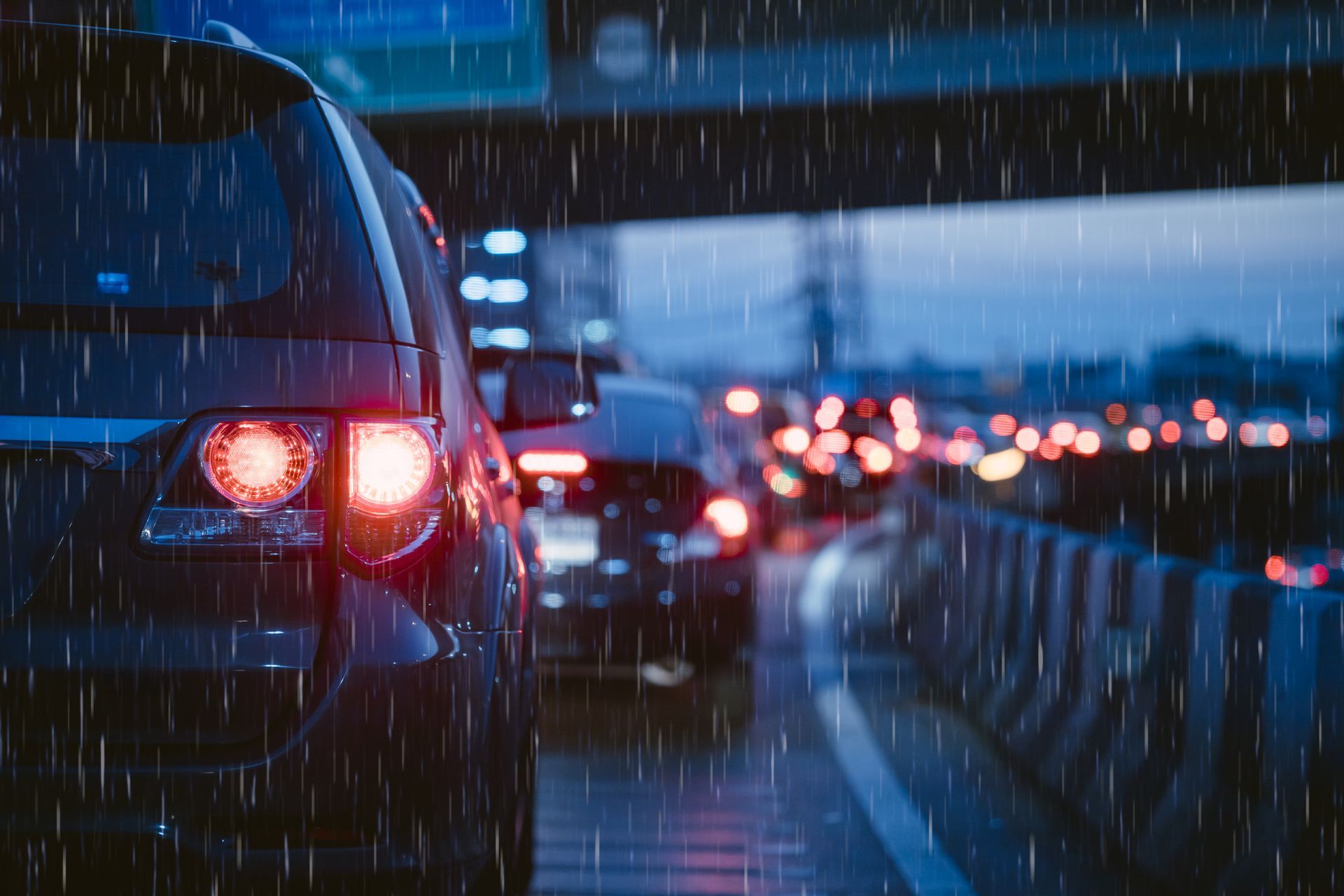 Cars in traffic during a rainstorm, illuminated taillights, blurred lights in the distance.