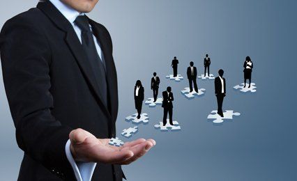 Graphics of people in black, standing on white jigsaw pieces that appear to be floating off the outstretched hand of a man in suit and tie