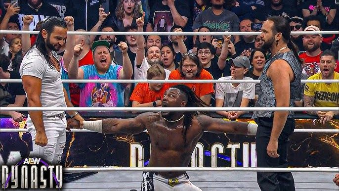 Two men are standing in a wrestling ring with a crowd watching.