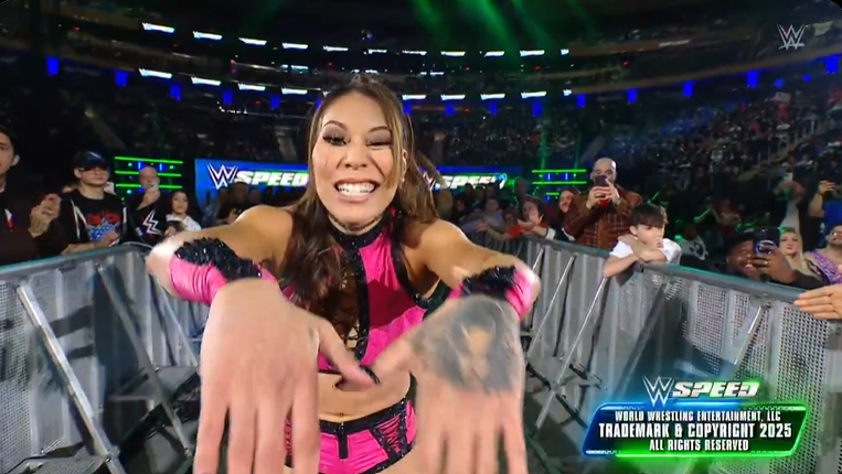 A woman in a pink wrestling outfit is sitting in a ring.