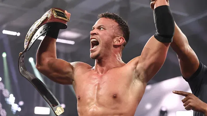 A shirtless wrestler is holding a championship belt over his head.