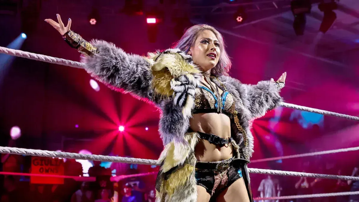 A female wrestler is standing in a wrestling ring with her arms outstretched.