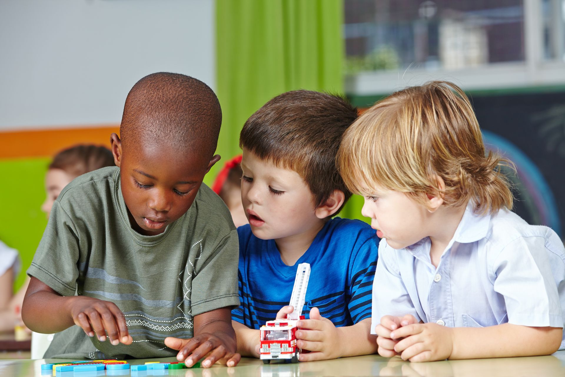 Three young boys are sitting at a table playing with toys.