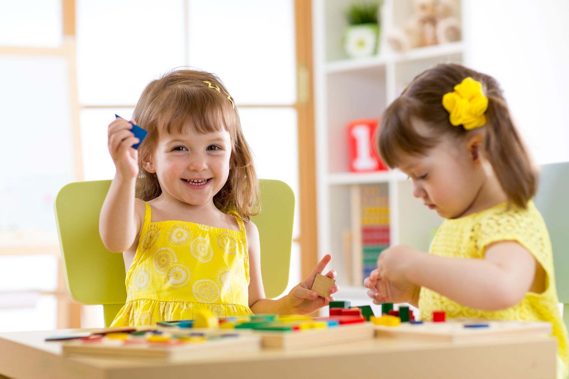 Two little girls are playing with lego blocks at a table.