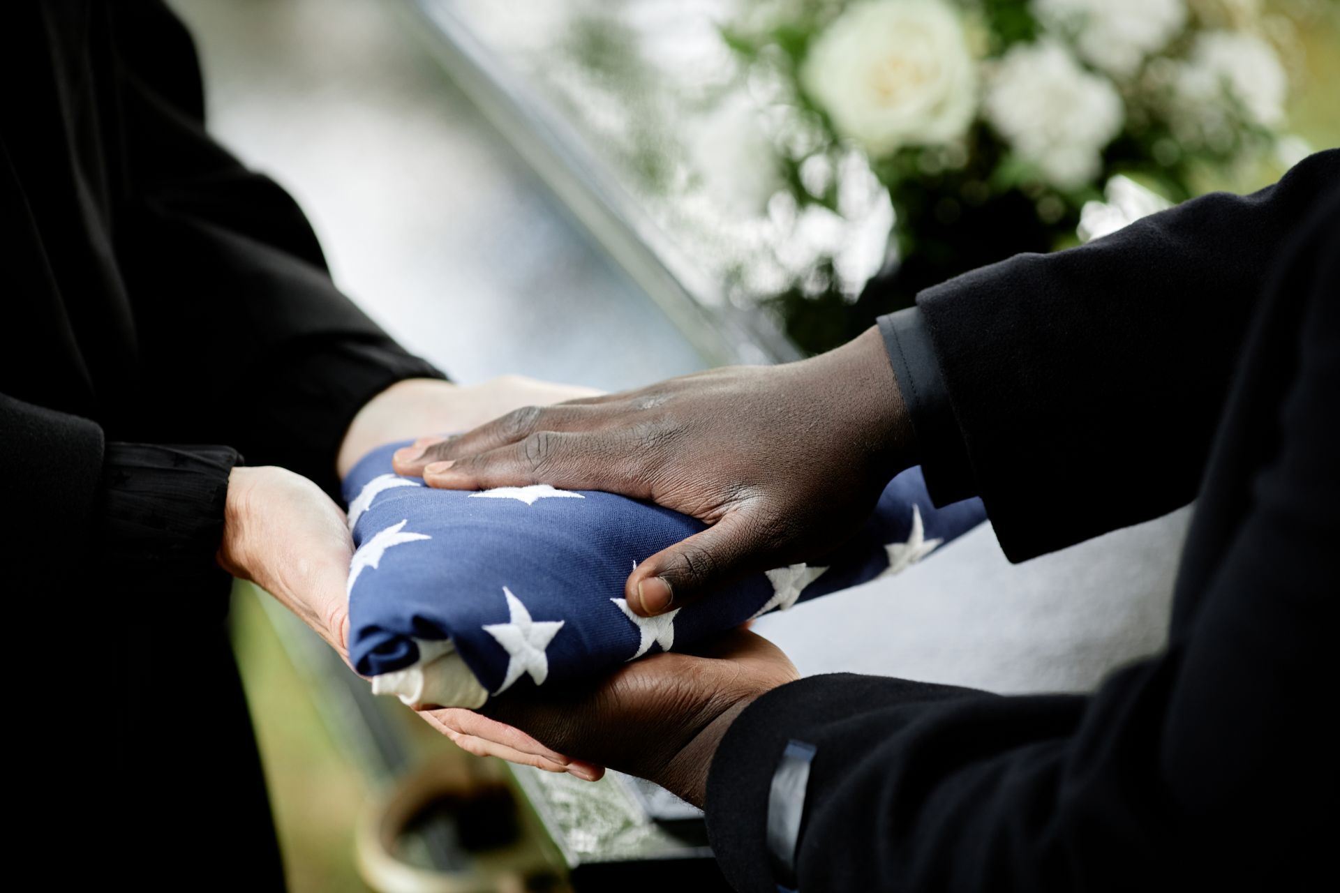 Hands folding a folded American flag, white flowers in the background.