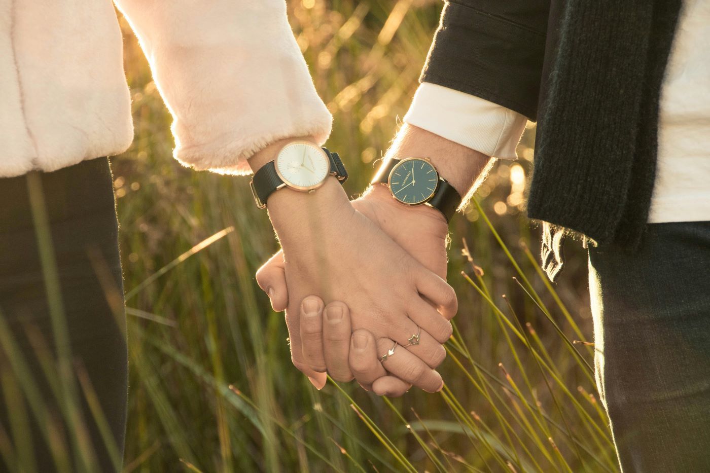 Two people holding hands, wearing watches, with sunlight in the background.