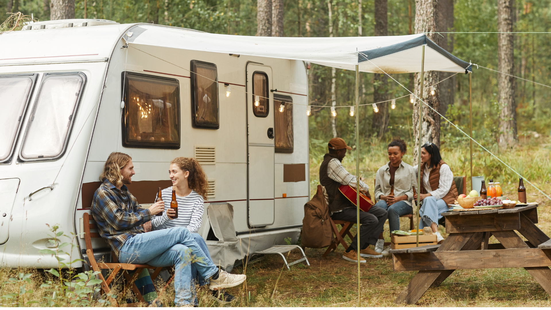 A group of people are sitting at a picnic table in front of a trailer.