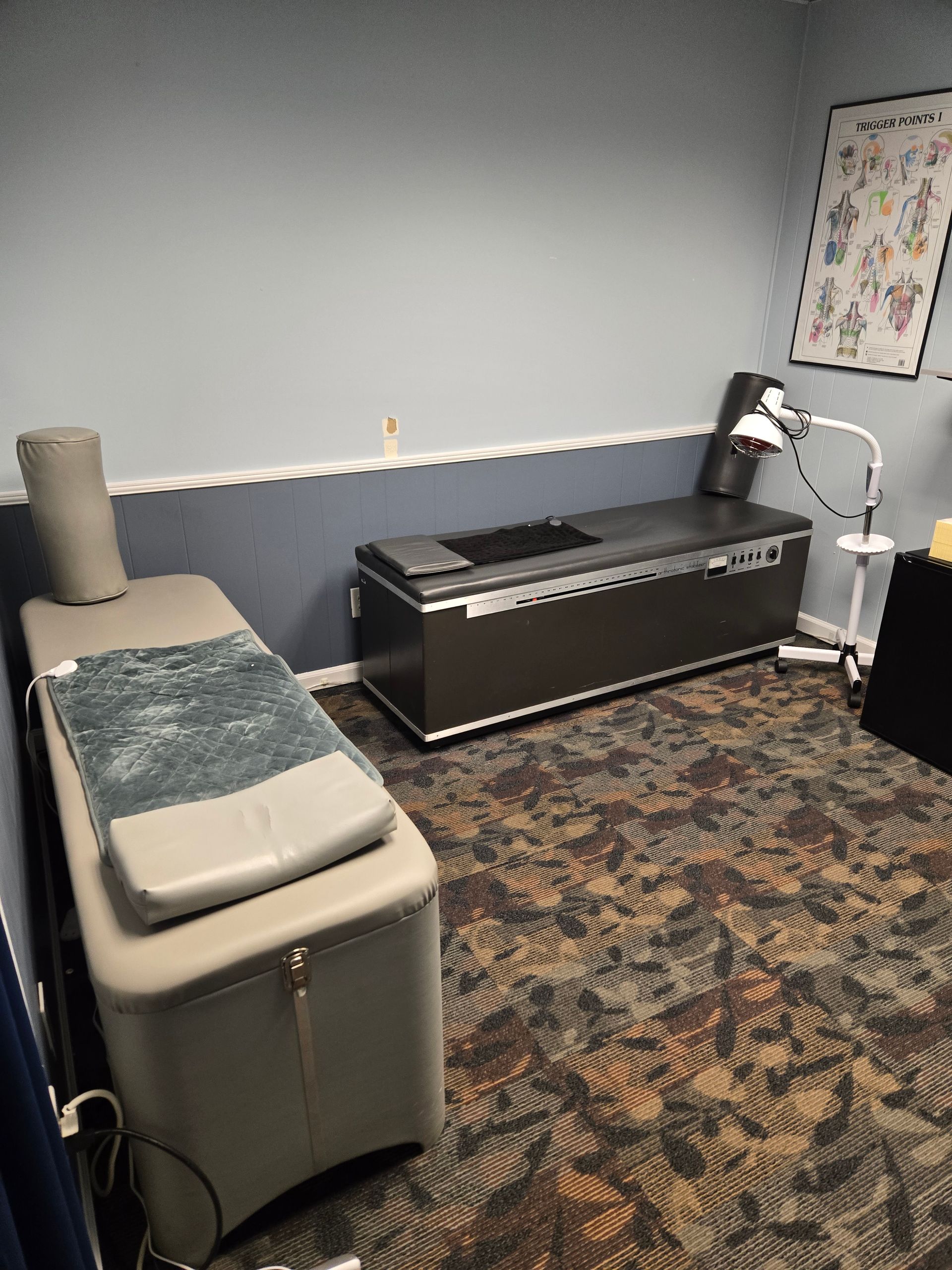 A room with treatment tables, burgundy curtains, and an evolution silhouette on the wall.