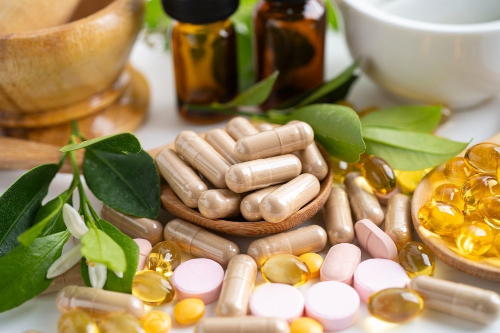 Supplements in capsules, pills, and softgels, with green leaves, essential oil bottles, and a mortar and pestle.