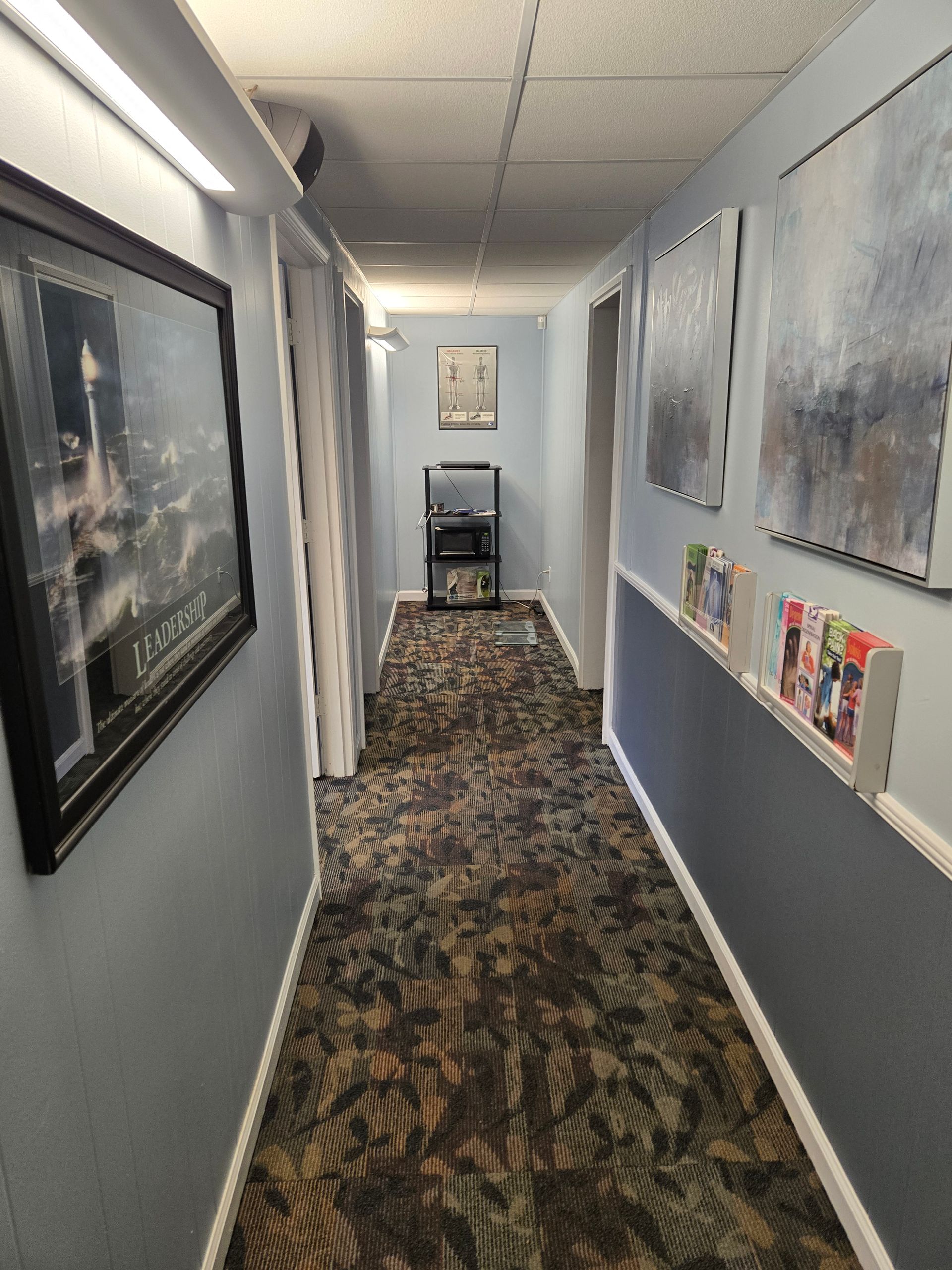 Chiropractor's office: patient on adjustable table, black chair, desk with laptop, potted plant, and window.