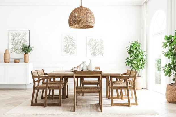 Dining room with wooden table, chairs, and woven pendant light. White walls, plants, and artwork.