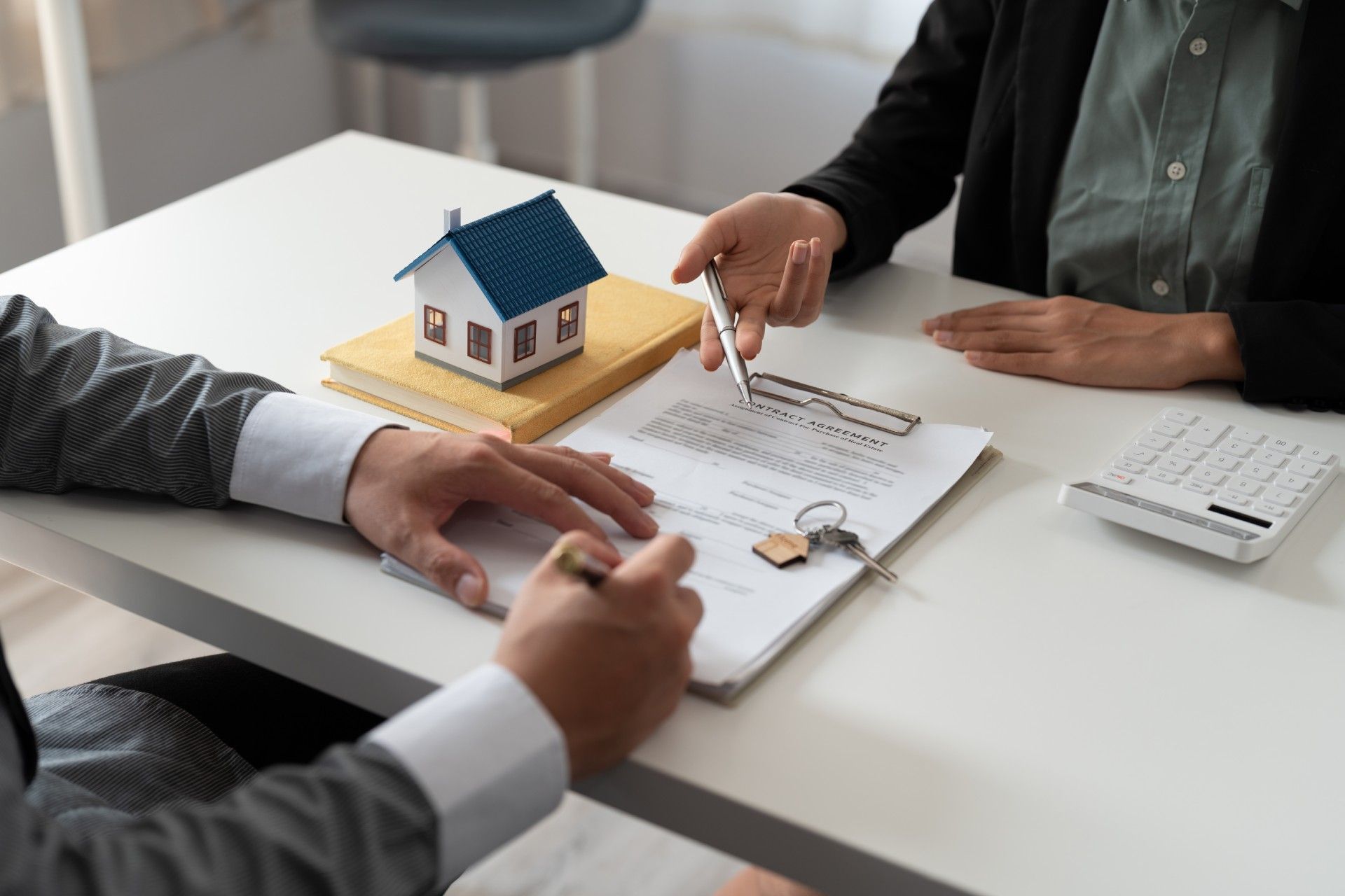 Two people at a table reviewing real estate paperwork with a miniature house and keys.