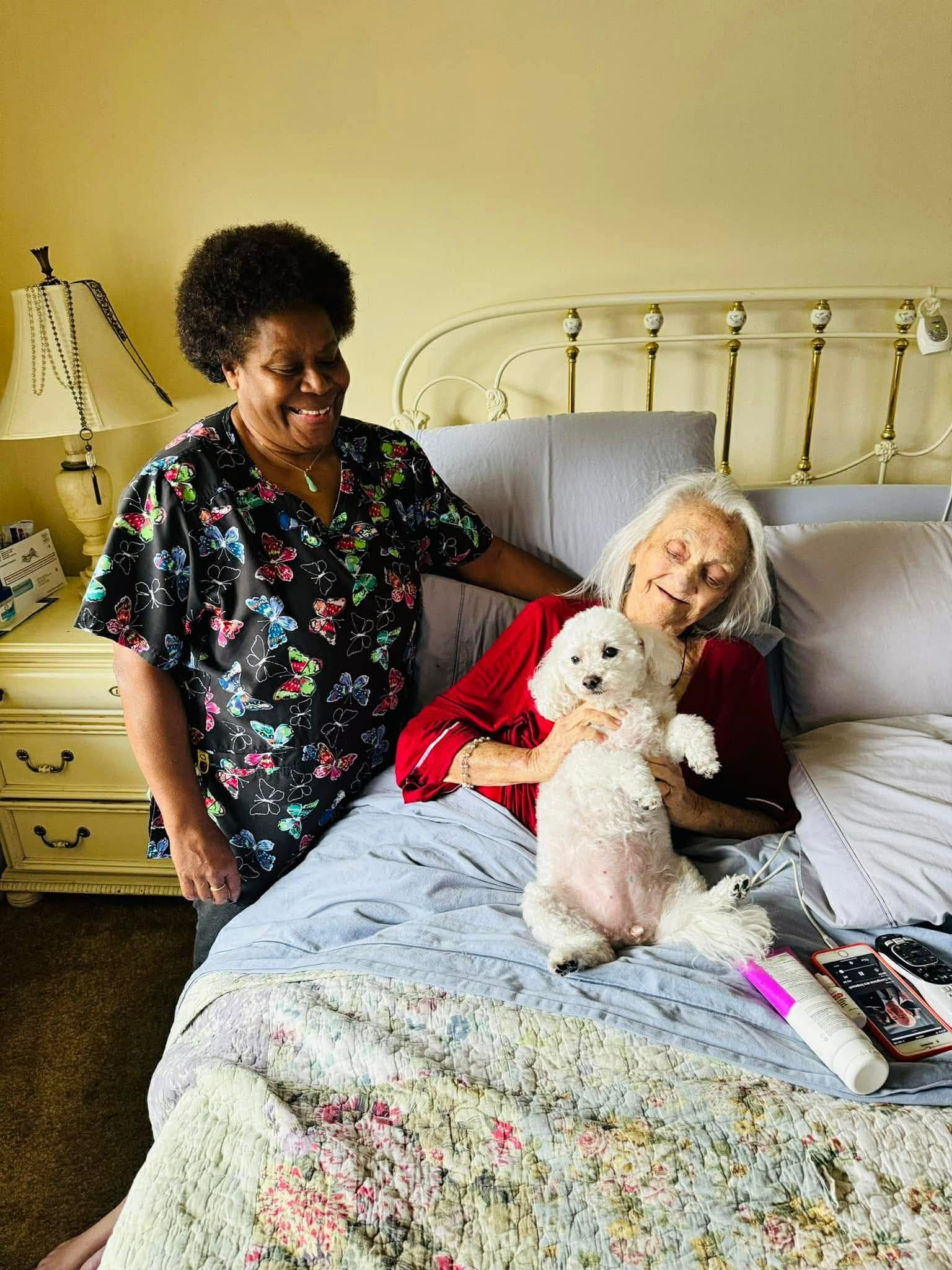 Caregiver offers a drink to an elderly person seated on a couch.