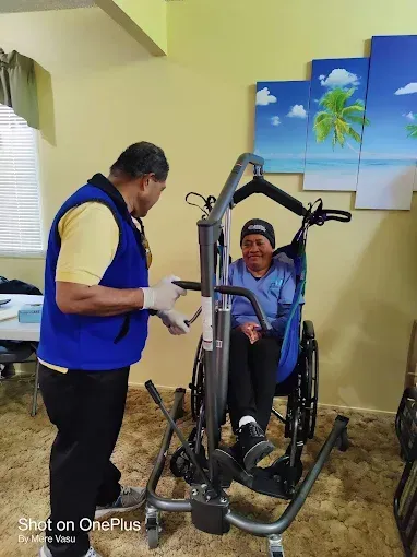 Caregiver assists a person in a wheelchair with a lift in a room.