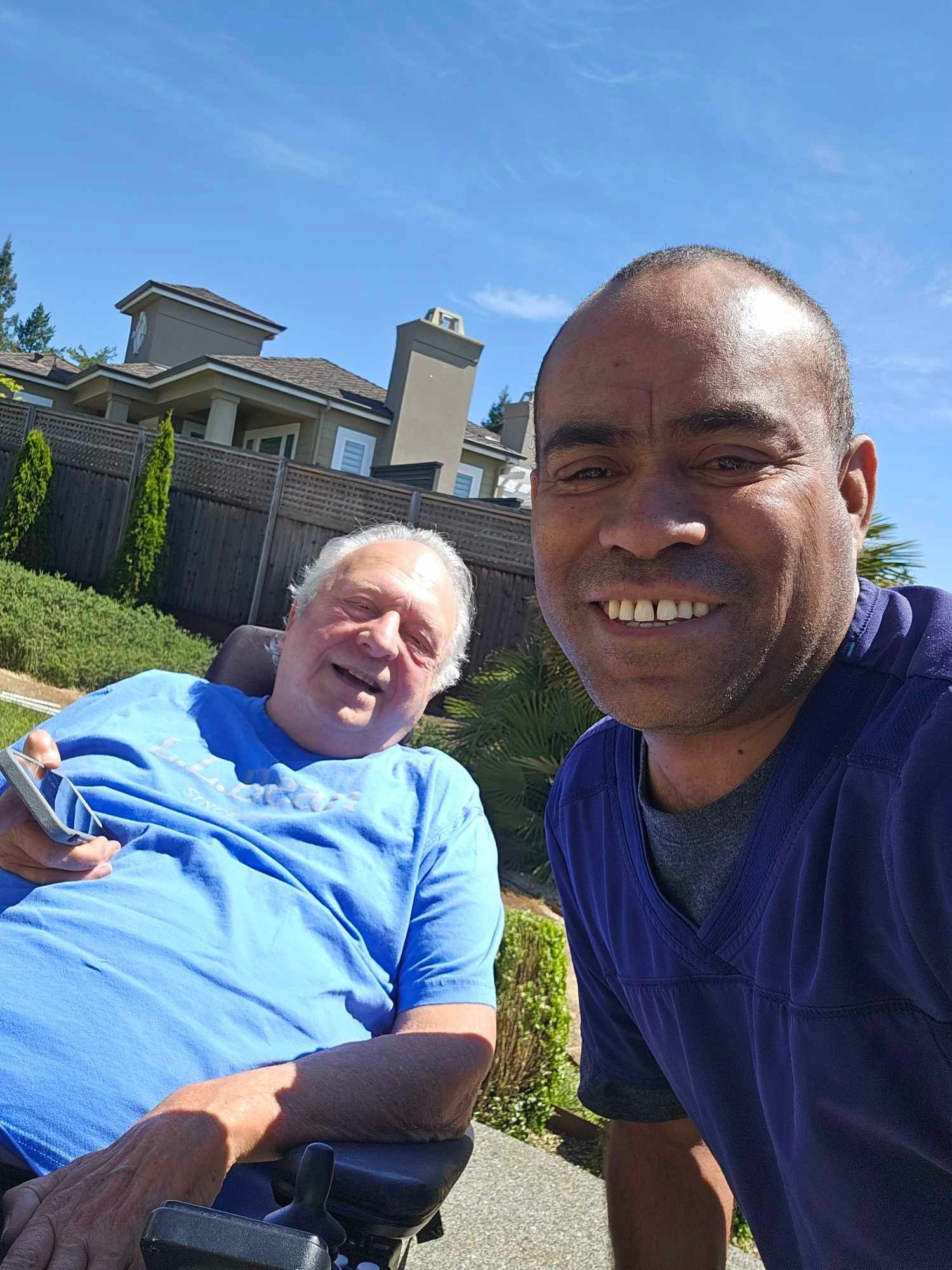 A person in a wheelchair and another person converse on a bench outside a building.