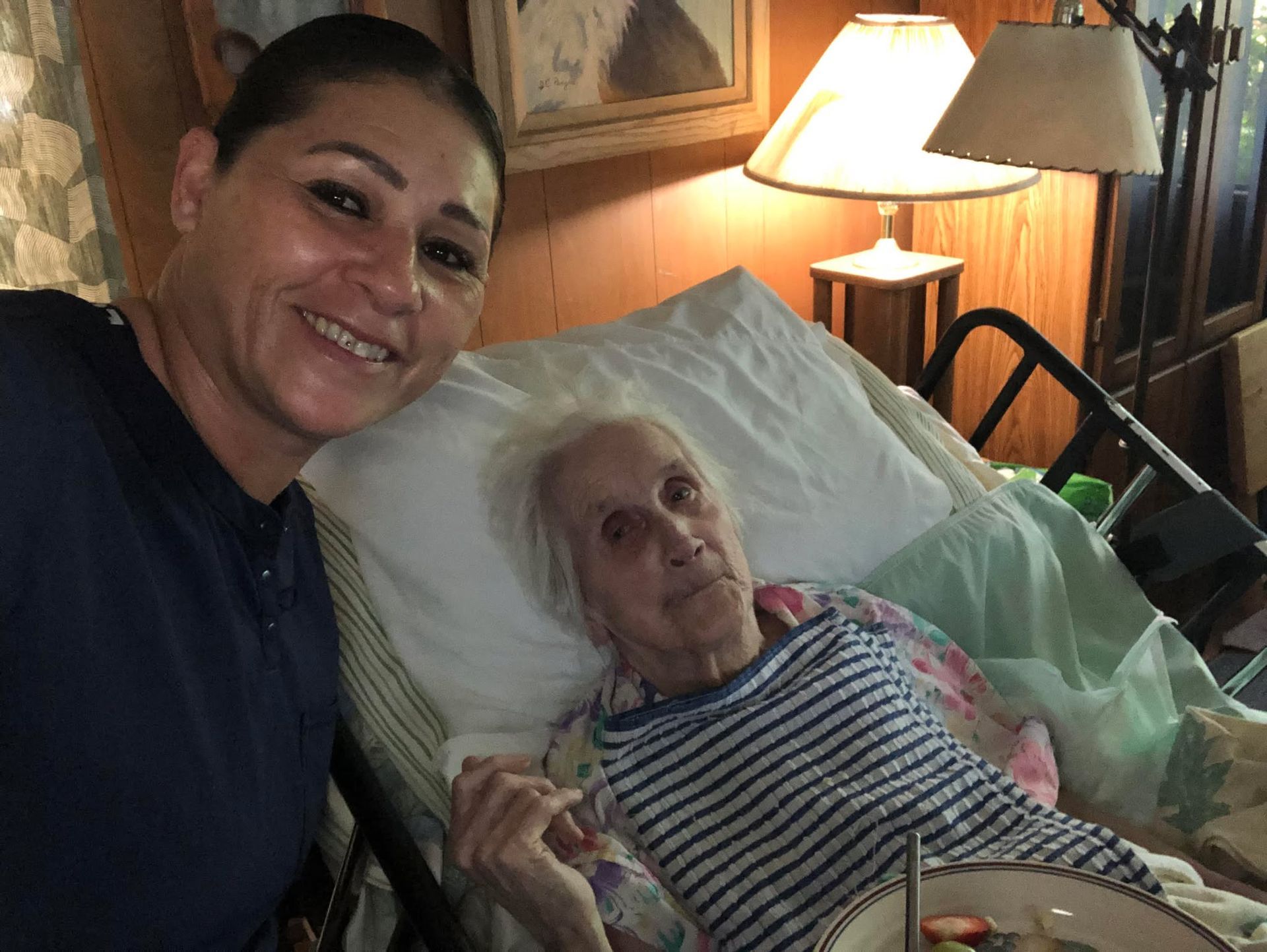 Person taking medication from a pill organizer, offered a glass of water by another person.