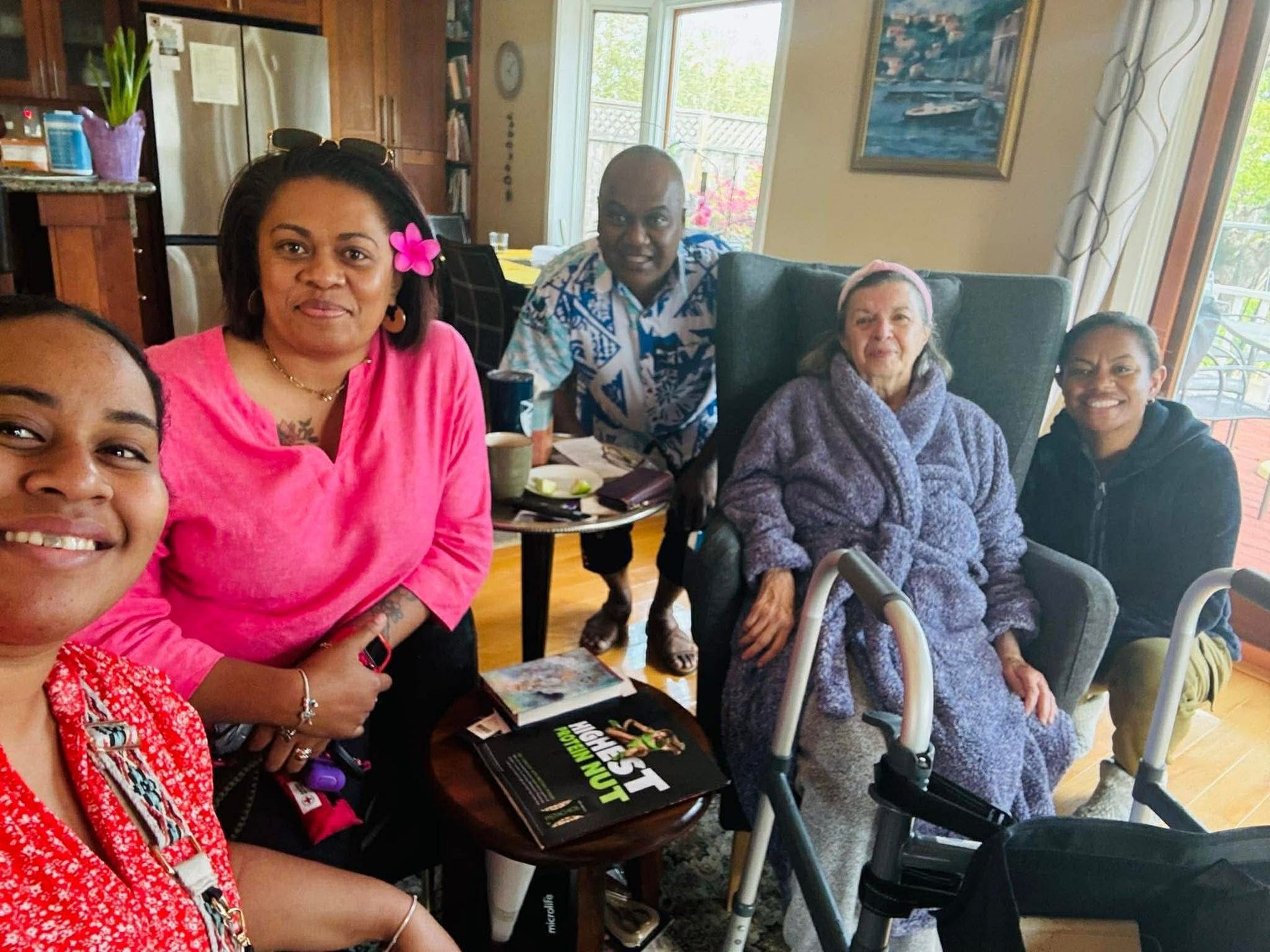 Four people in blue shirts stand by a car outdoors; trees and grass in the background.