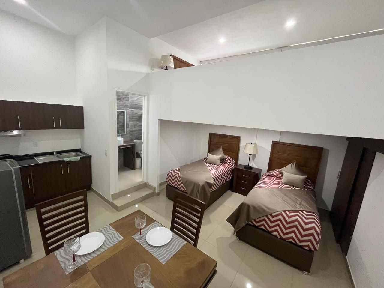 Un apartamento tipo estudio con dos camas, cocina, mesa de comedor y baño.
