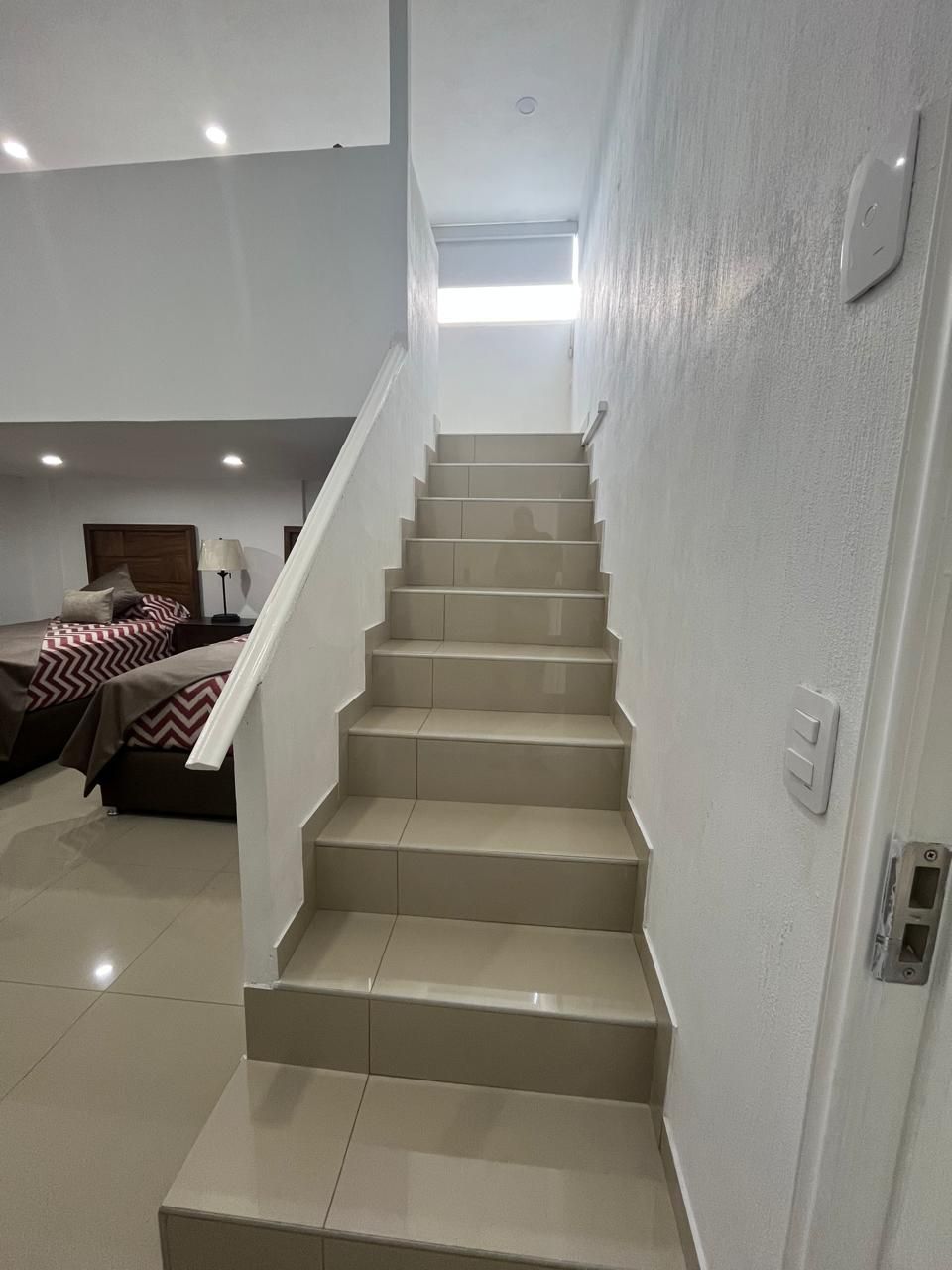 Escalera que sube a una ventana. Escalones de baldosas con paredes y barandilla blancas. Vista de dos camas.