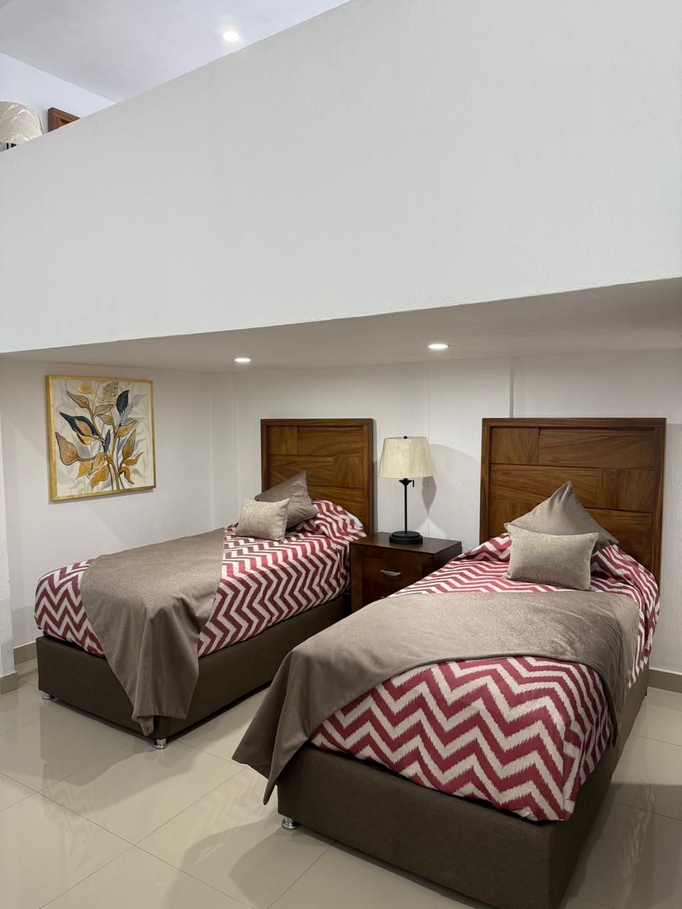 Dos camas individuales con cabeceros marrones y mantas rojas con estampado en zigzag en una habitación blanca.